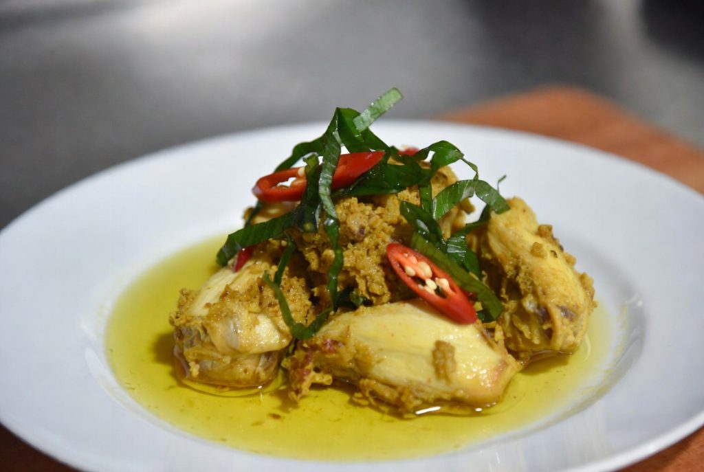 Ayam Woku Belanga dengan kuah kuning kental dan daun kemangi segar